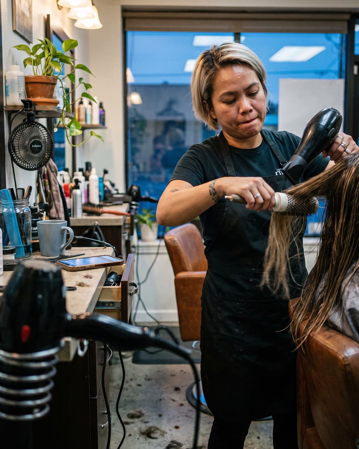 A stylist blow-drying a client’s hair in her salon